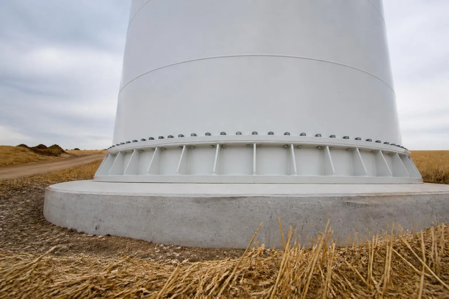 Un mât d'éolienne terrestre vu du pied, ses pales immobiles au-dessus d'un champ de blé coupé