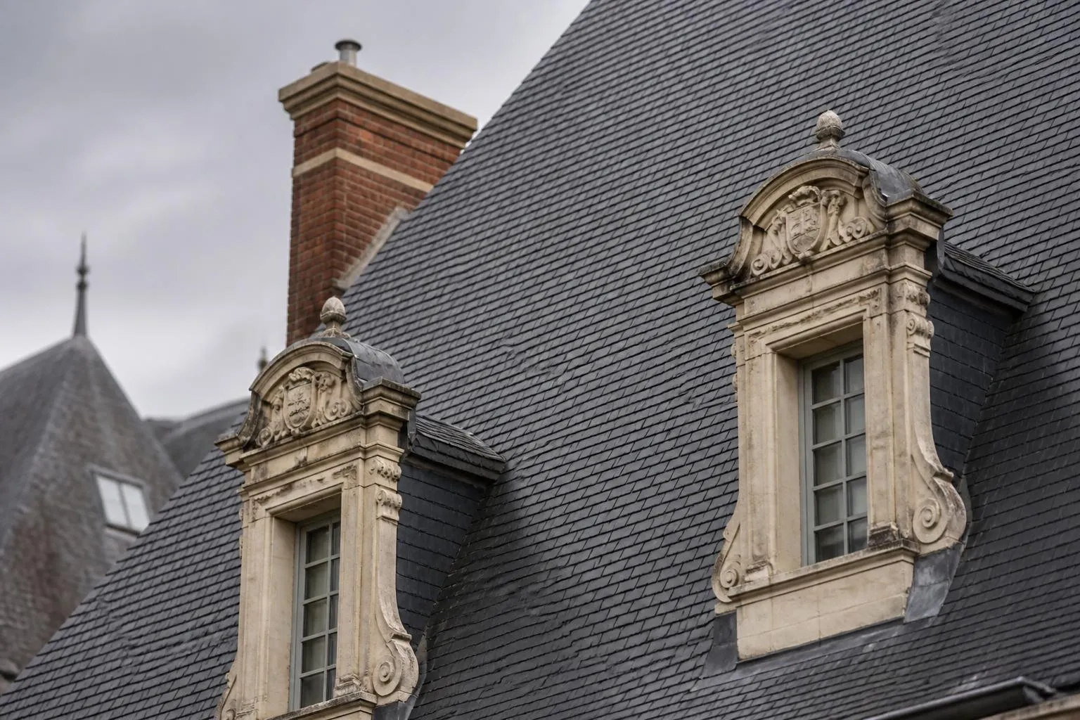 Toiture d’ardoise, lucarnes de pierre et souche de cheminée d’un corps de logis ancien, vues de près