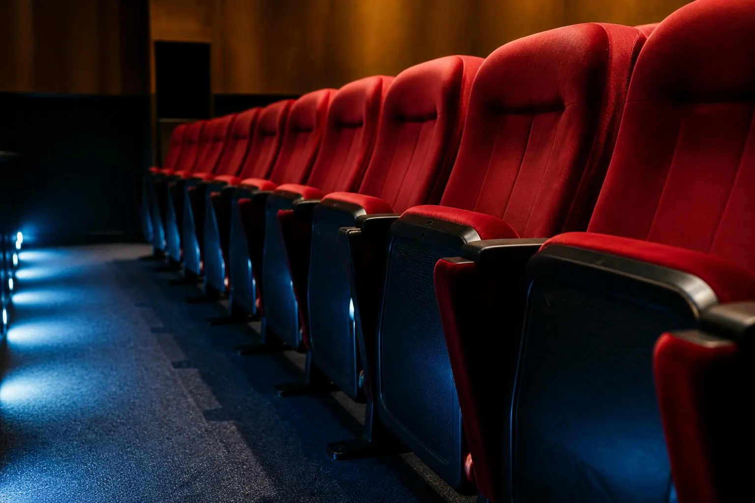 Rangée de fauteuils rouges rabattus dans une salle de cinéma vide, éclairée par les veilleuses au sol