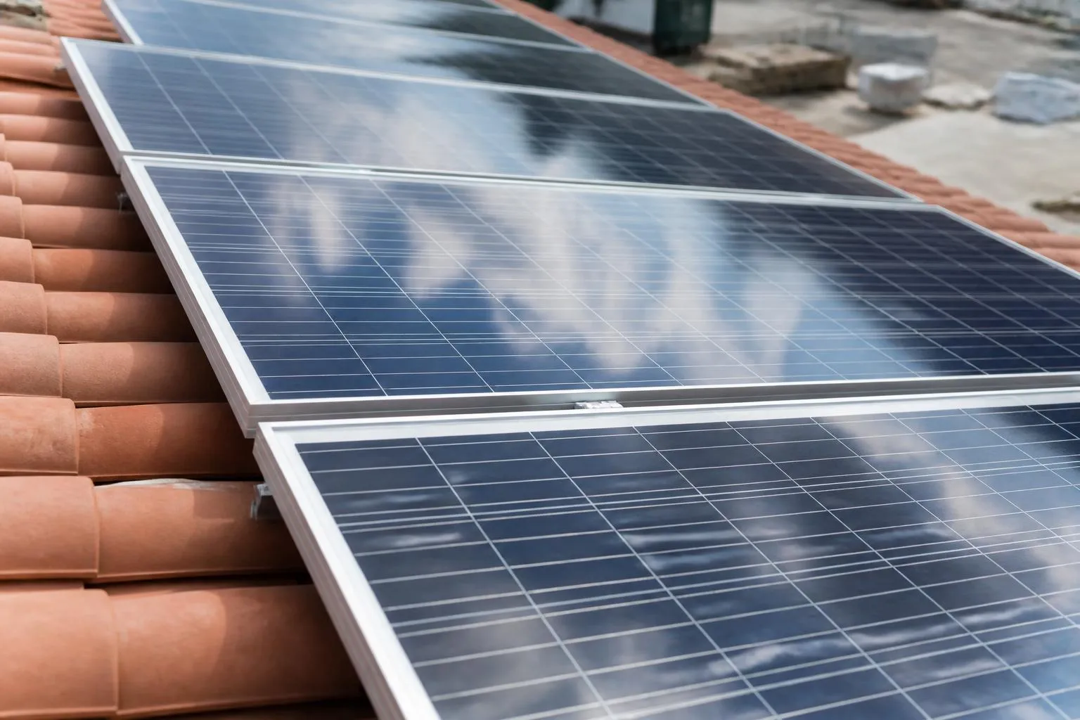 Des modules photovoltaïques alignés sur une toiture de tuiles, cadres d'aluminium et reflet du ciel.